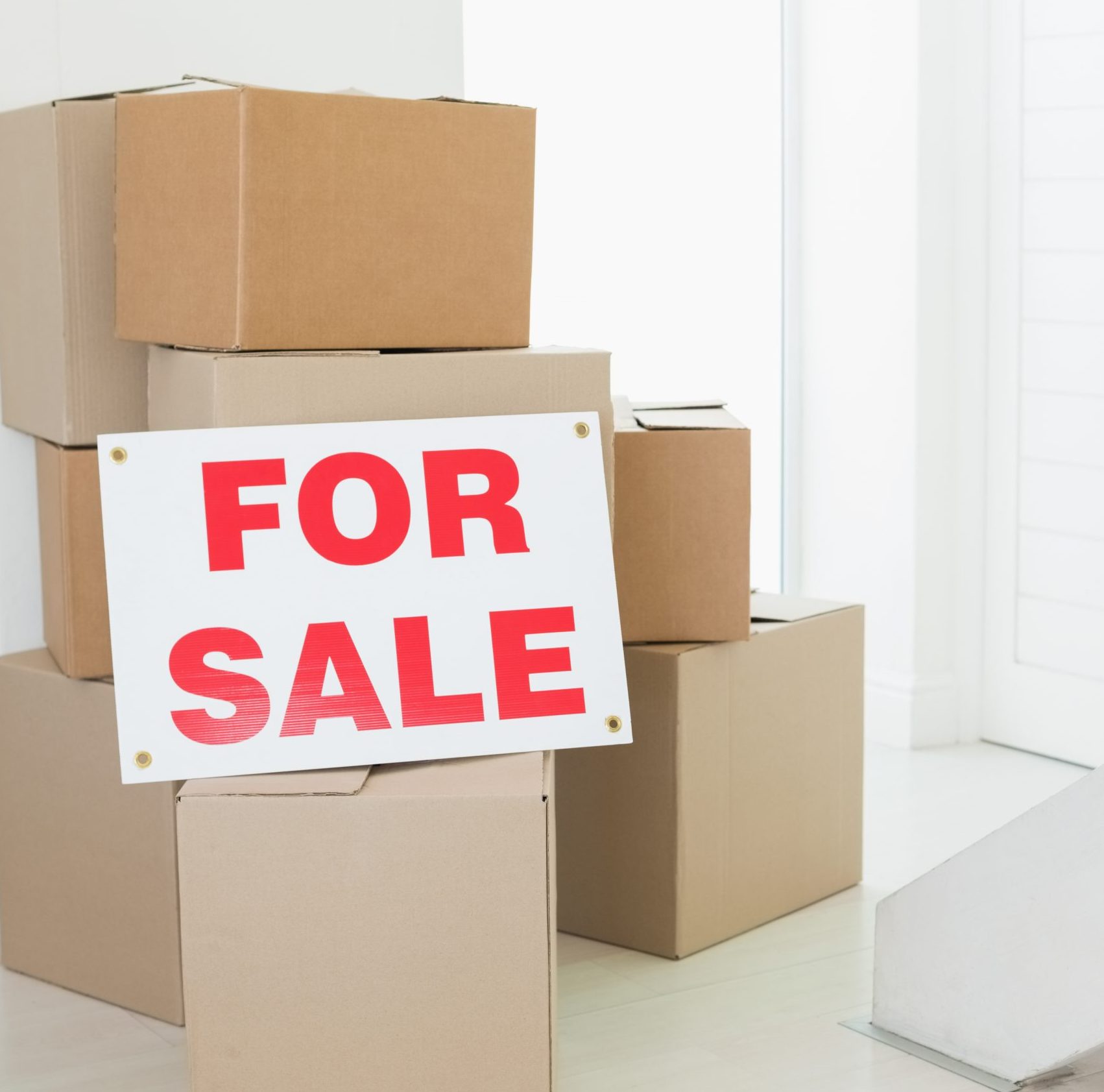 For sale sign with many cardboard boxes in an empty house